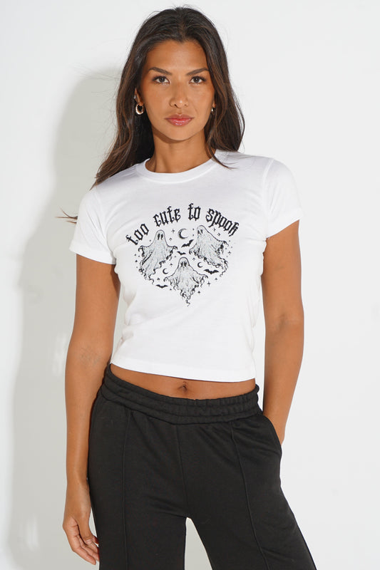 A woman modeling a white cropped short-sleeve t-shirt with a black graphic print of a winged heart and the text 'too cute to speak' on the front, paired with black sweatpants against a plain white background.