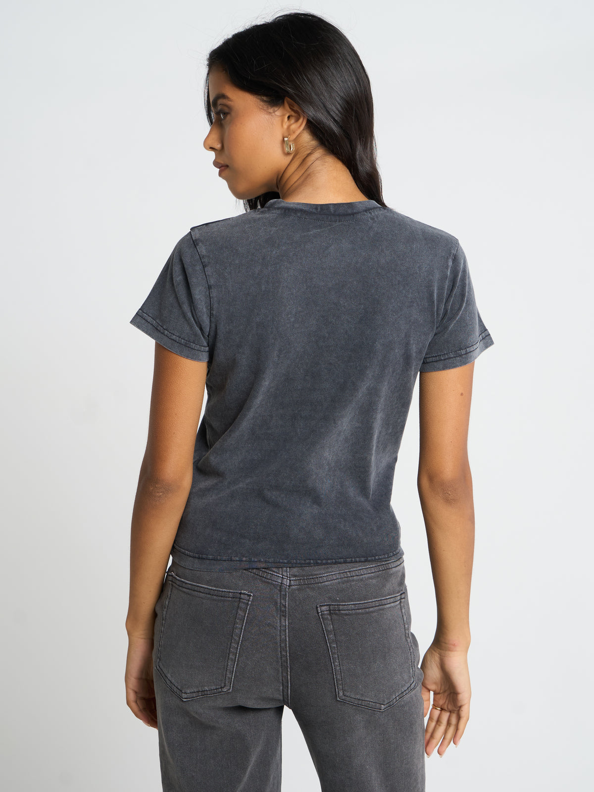 A woman shown from the back wearing a dark gray washed short-sleeve t-shirt and matching gray jeans against a light gray studio background.