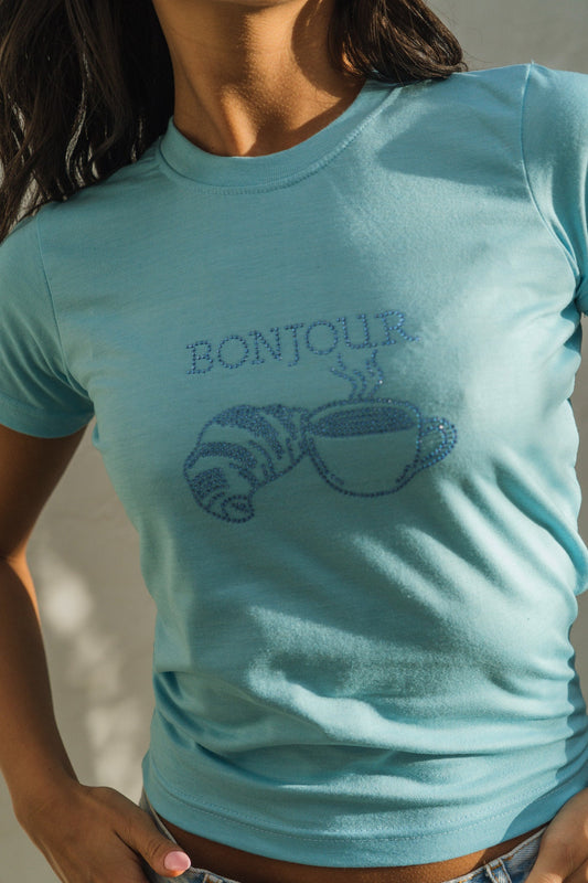 Model wearing a light blue rhinestone t-shirt with 'Bonjour' design.