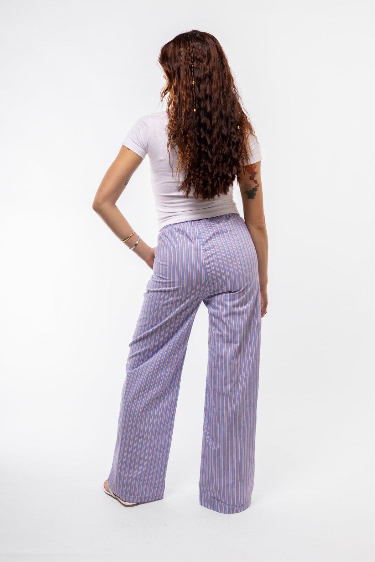 Blue vertically striped trousers, shown from the back to highlight flattering fall and loose fit.