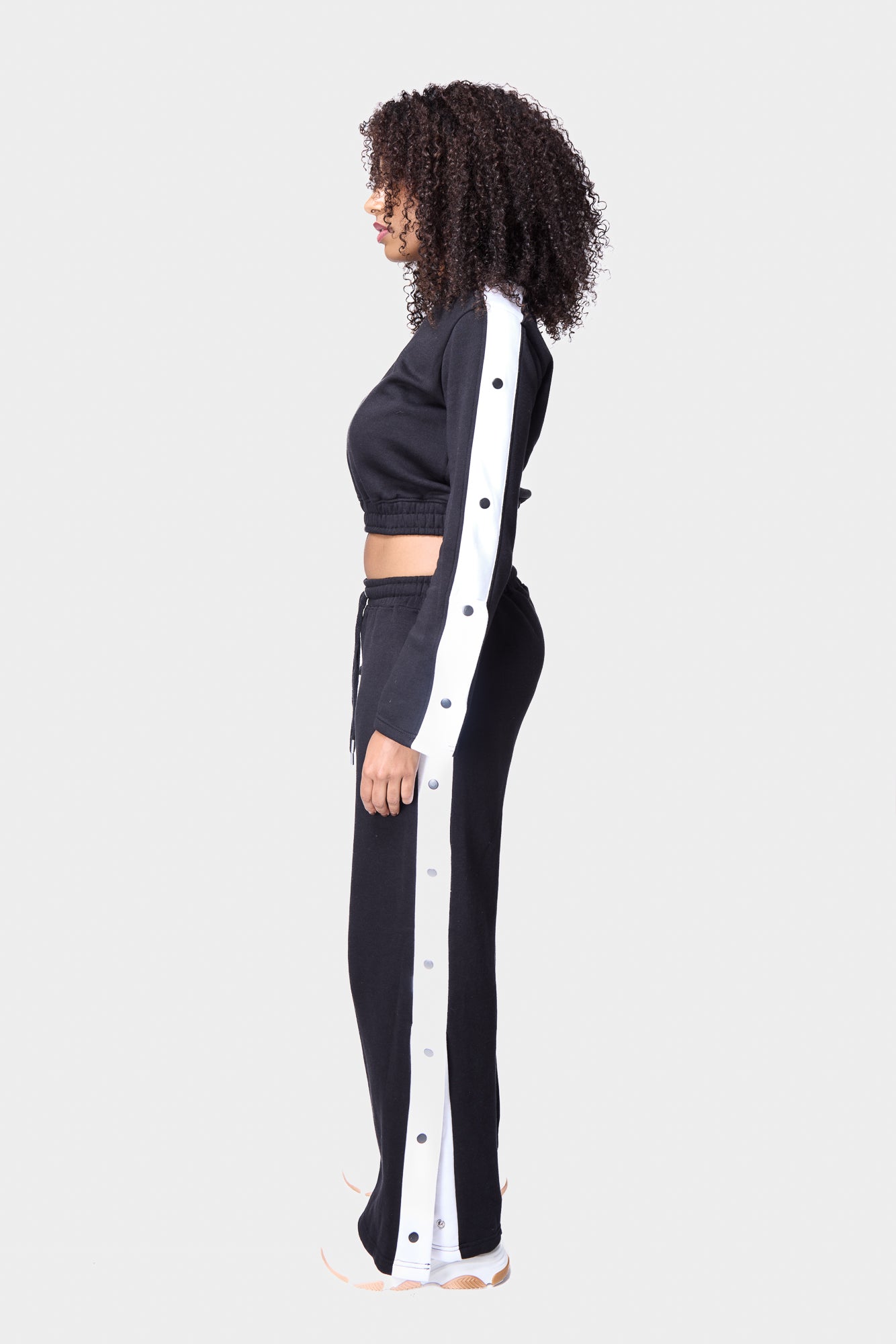 Black cropped track top with white snap buttons along the sleeves, creating a trendy and sporty look.