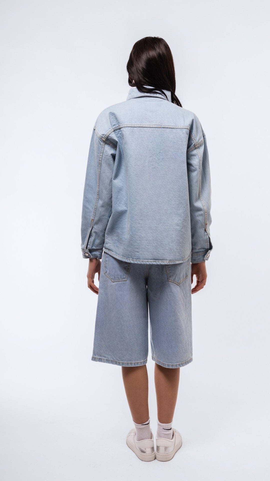 Rear shot of longline jorts in faded denim with relaxed fit and raw hem finish.