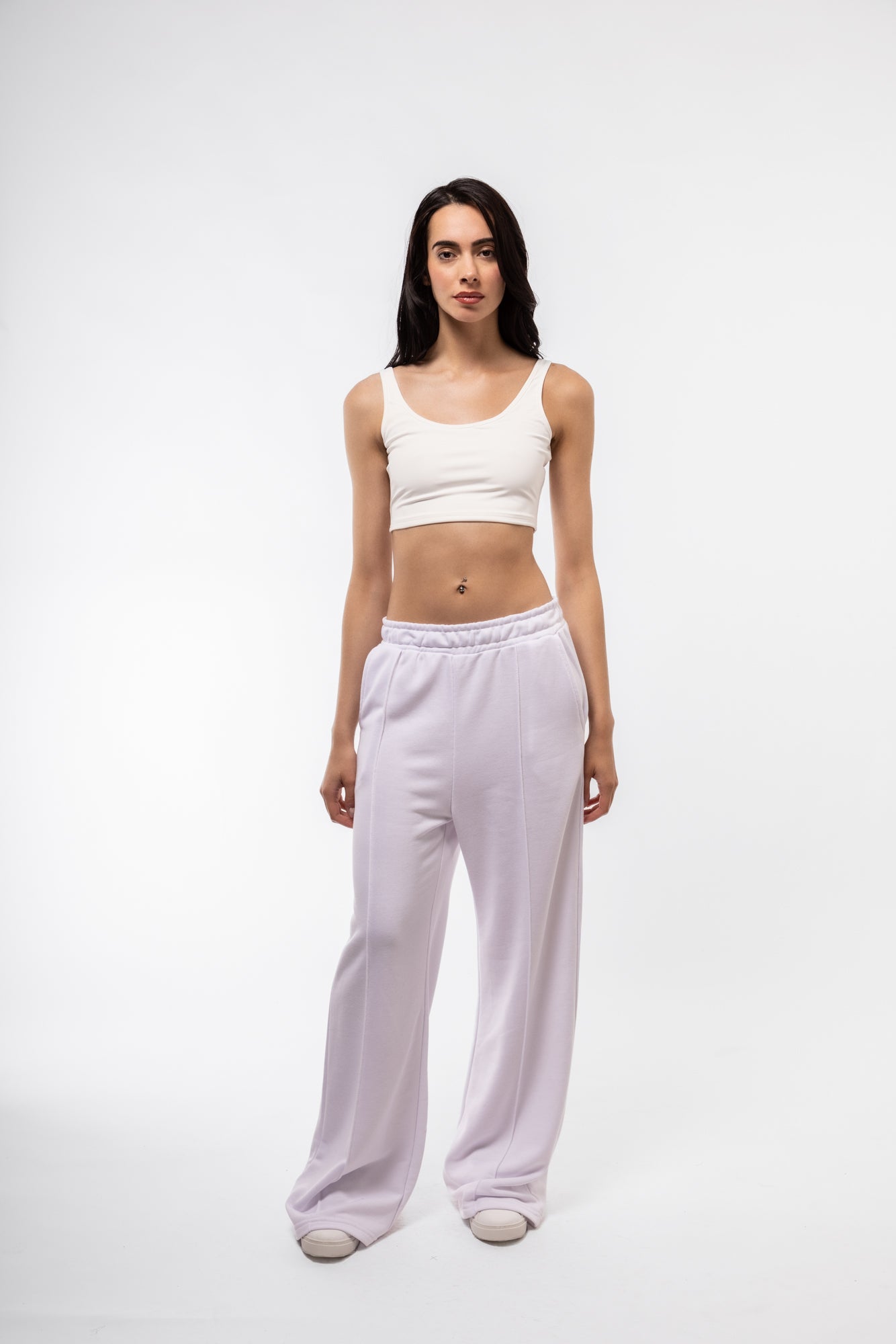 Woman wearing a white crop top and light purple pants on a white background
