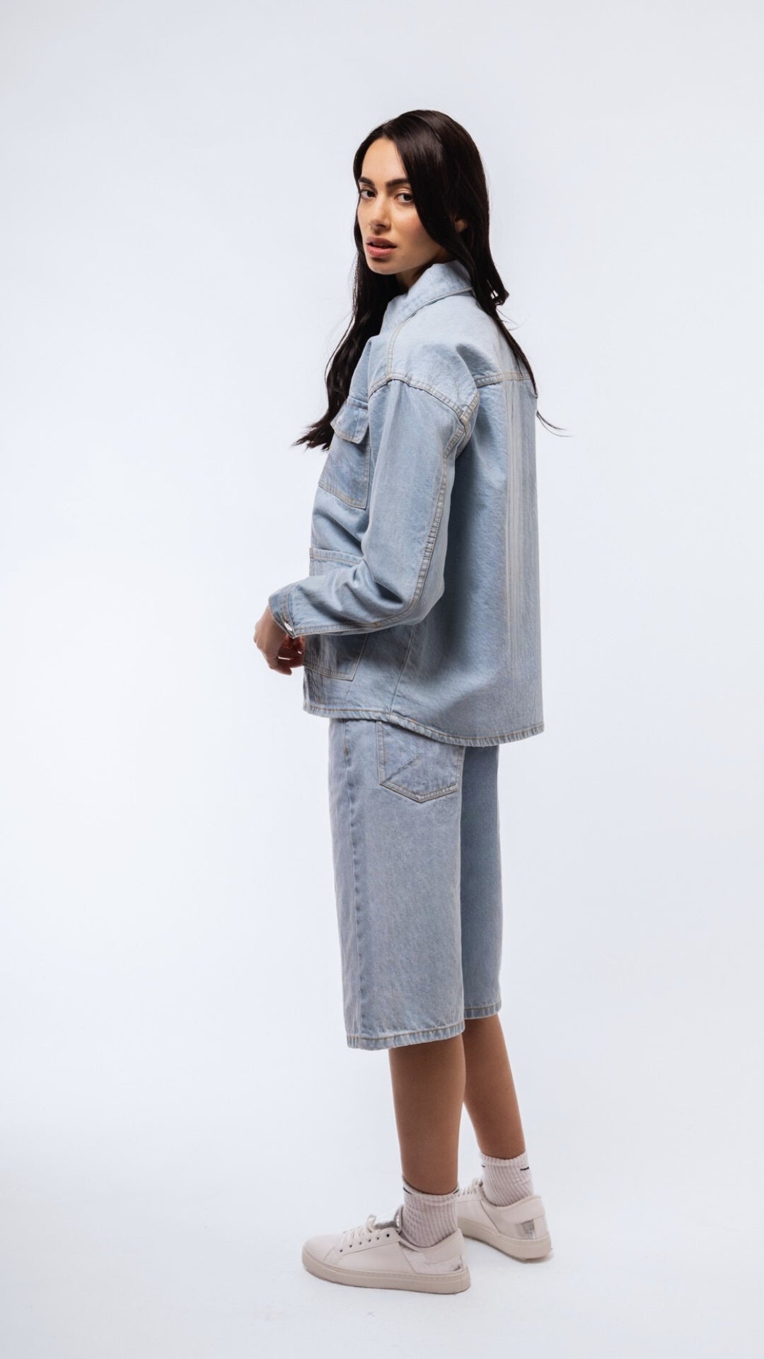 Side shot of light-wash denim longline shirt with cuffed sleeves and flowy silhouette.