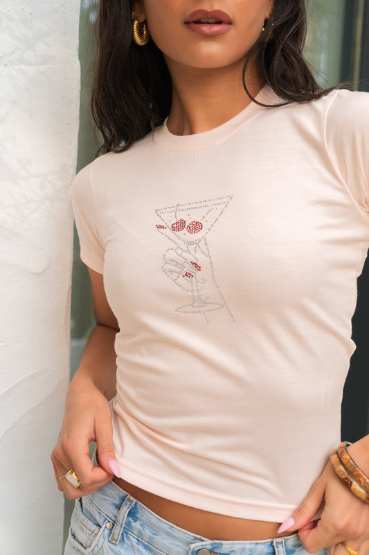 Woman wearing a beige t-shirt with a graphic design, standing against a white wall.