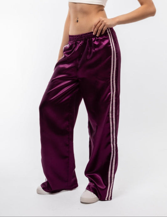 Woman wearing a white top and purple satin pants with white stripes on a white background
