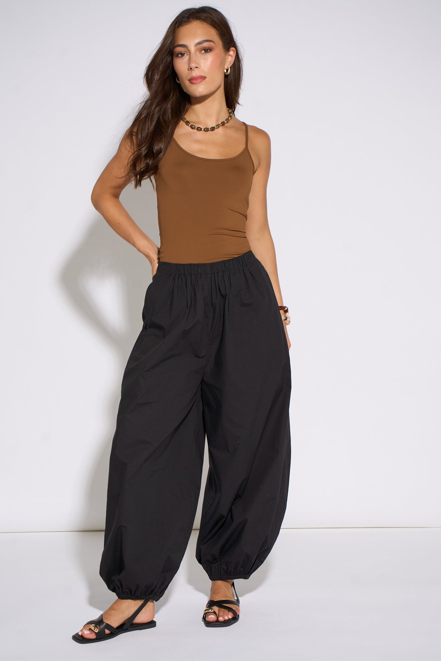 Woman wearing a brown tank top and black high-waisted pants on a white background