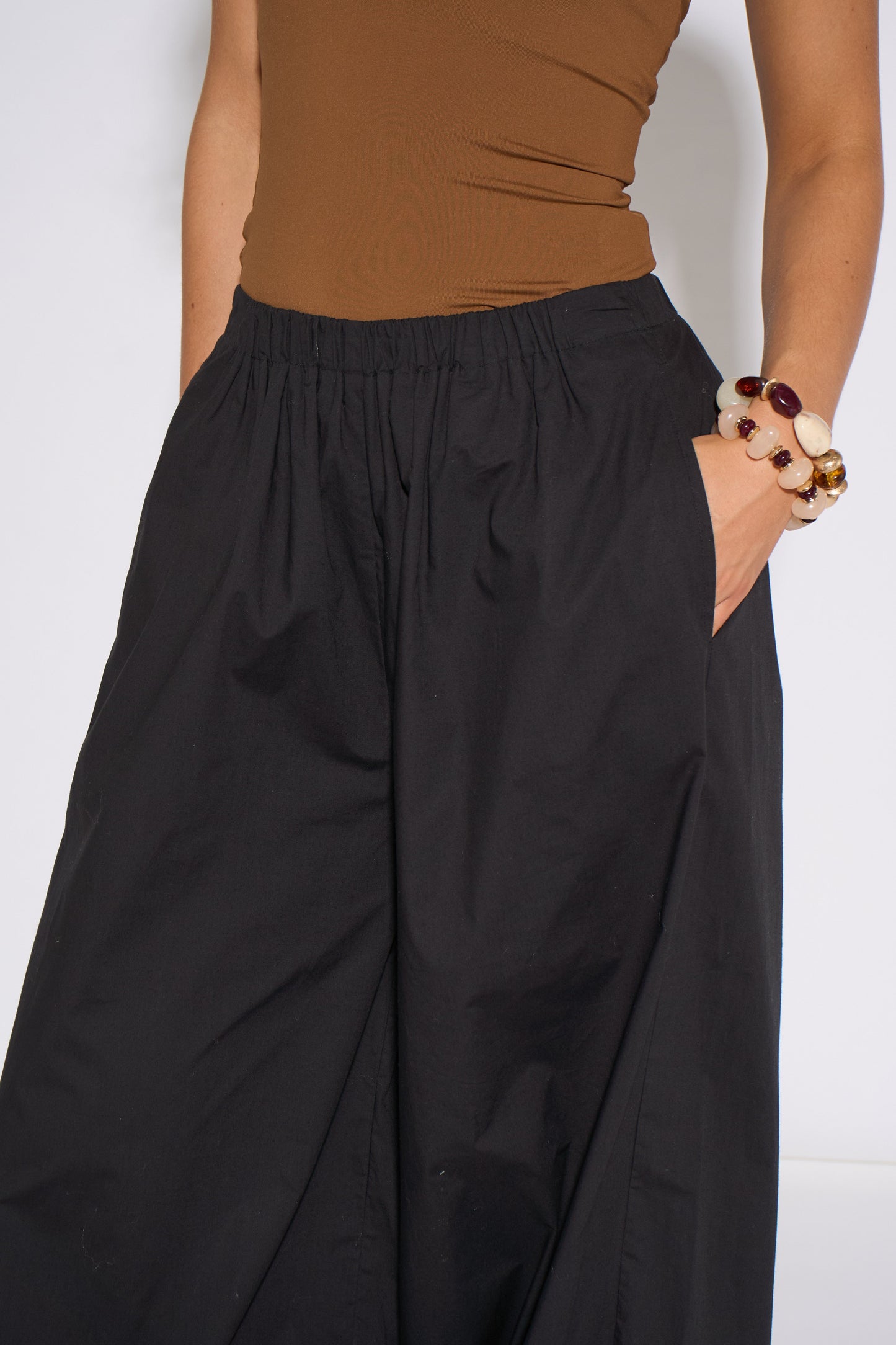 Person wearing a brown top and black wide-leg pants against a white background