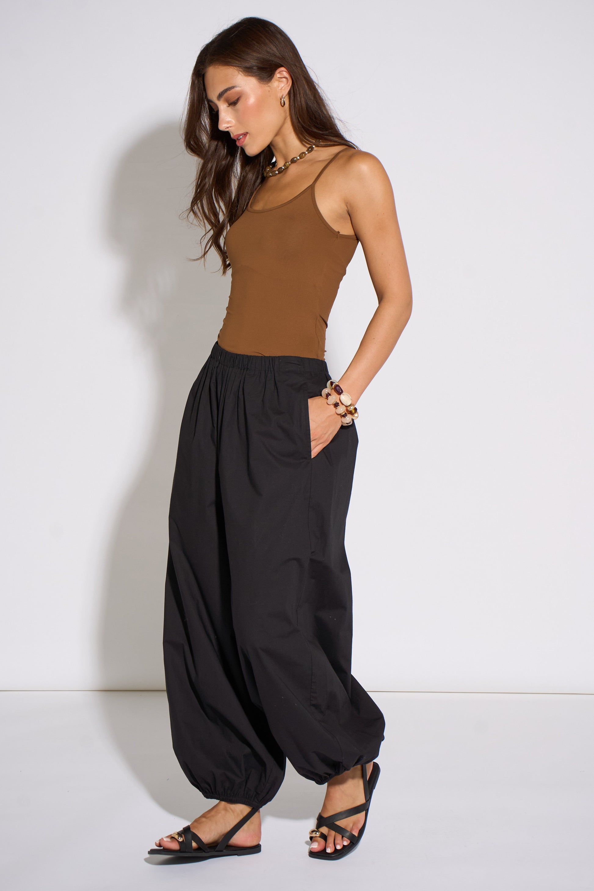 Woman wearing a brown tank top and black wide-leg pants against a white background