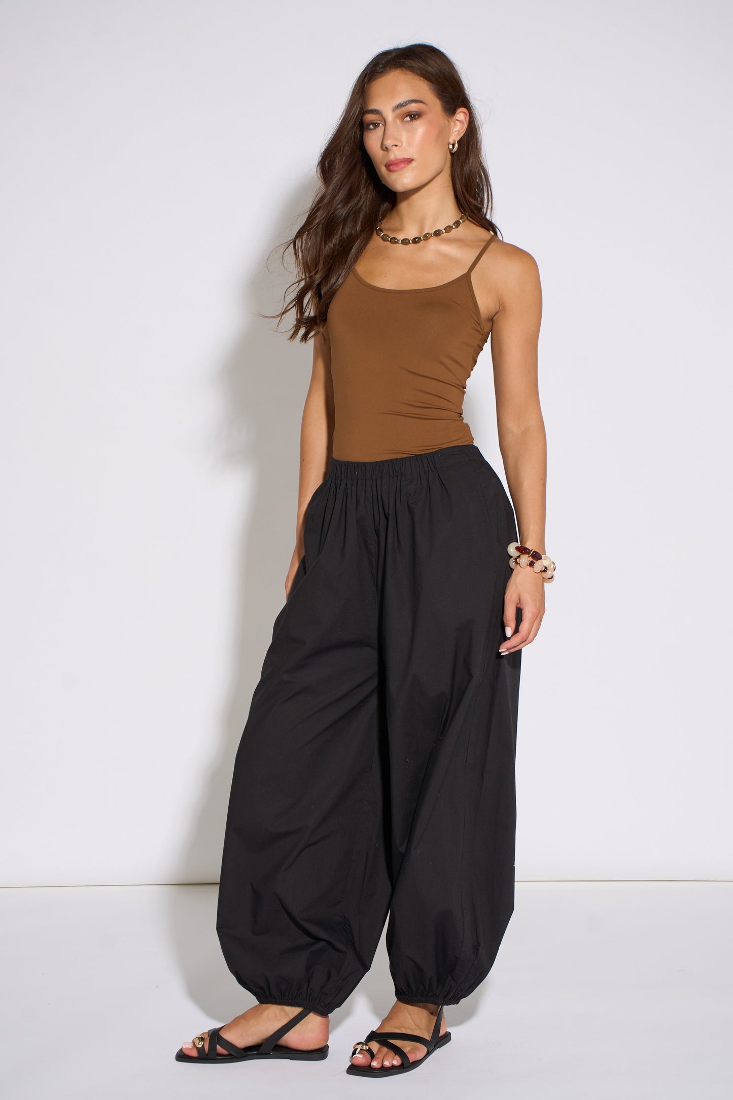 Woman wearing a brown top and black wide-leg pants against a white background