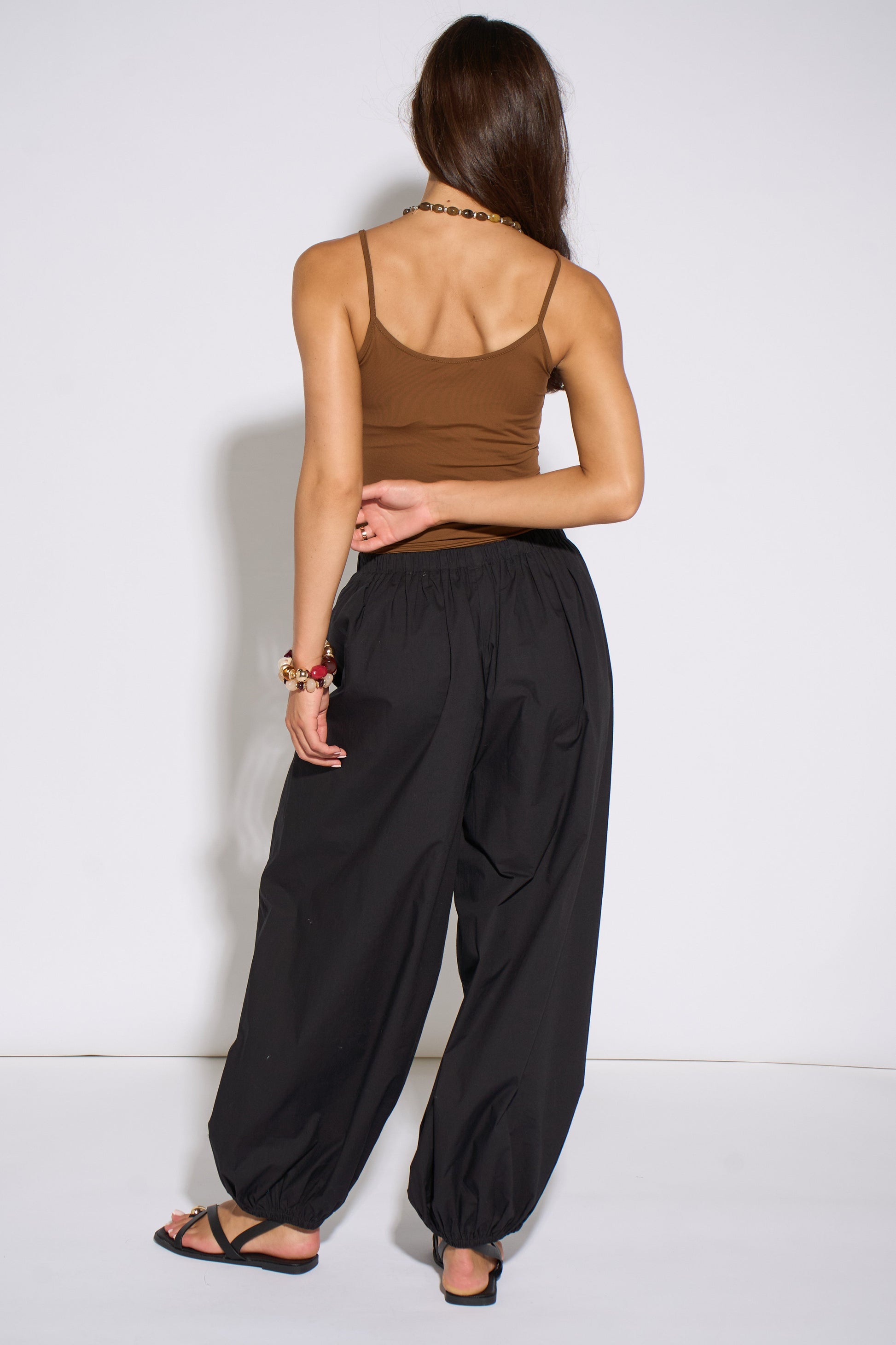 Woman wearing a brown tank top and black wide-leg pants against a white background