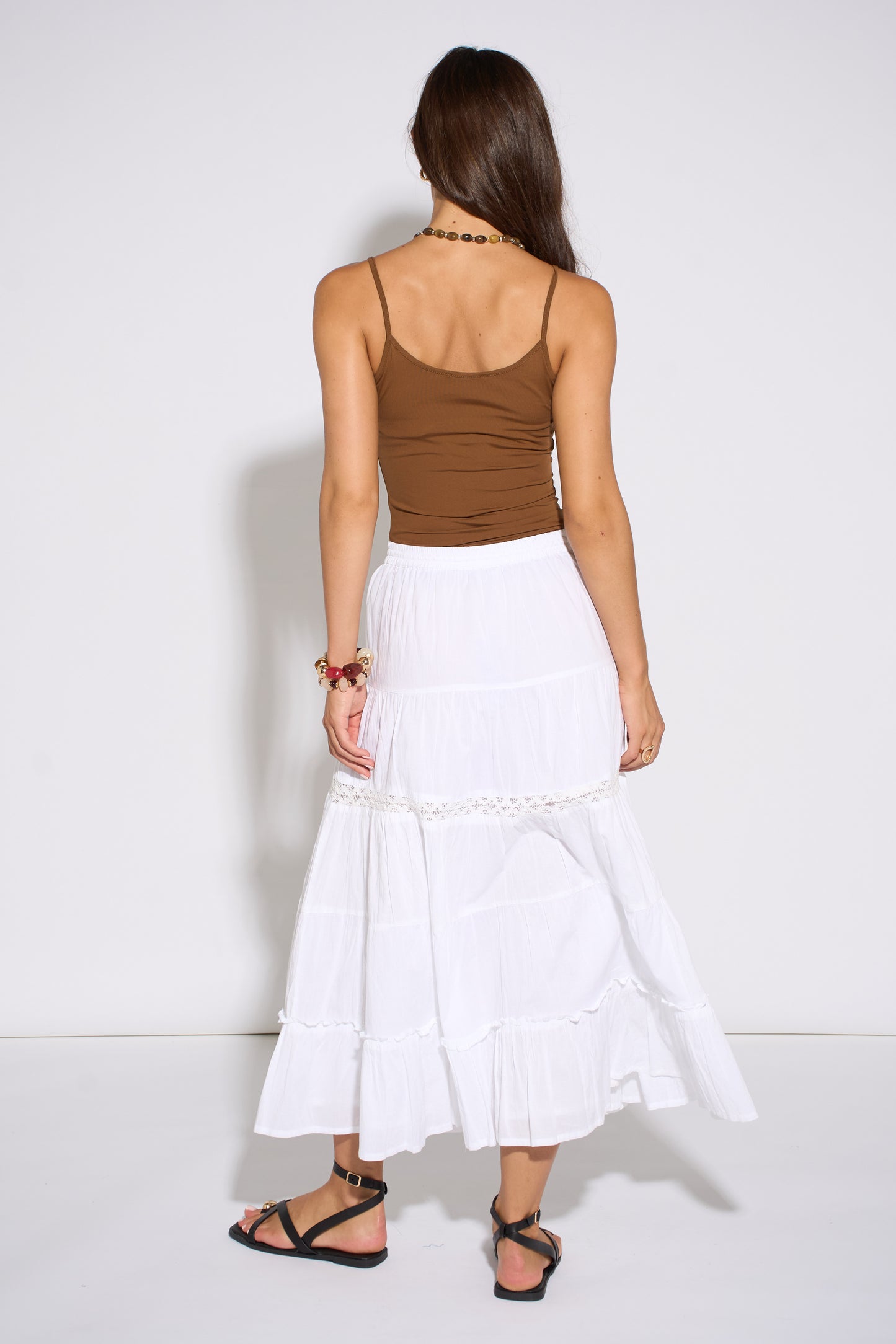 Woman wearing a brown top and white skirt against a white background