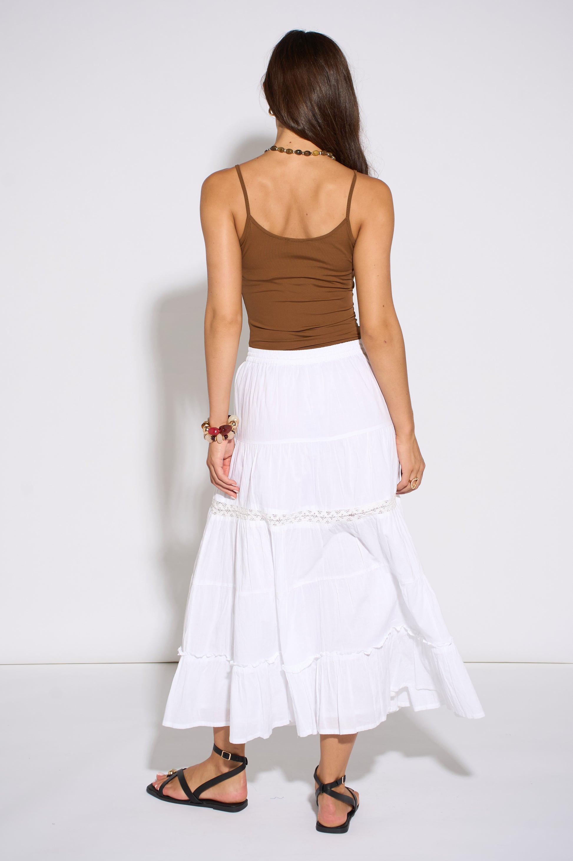 Woman wearing a brown top and white skirt against a white background