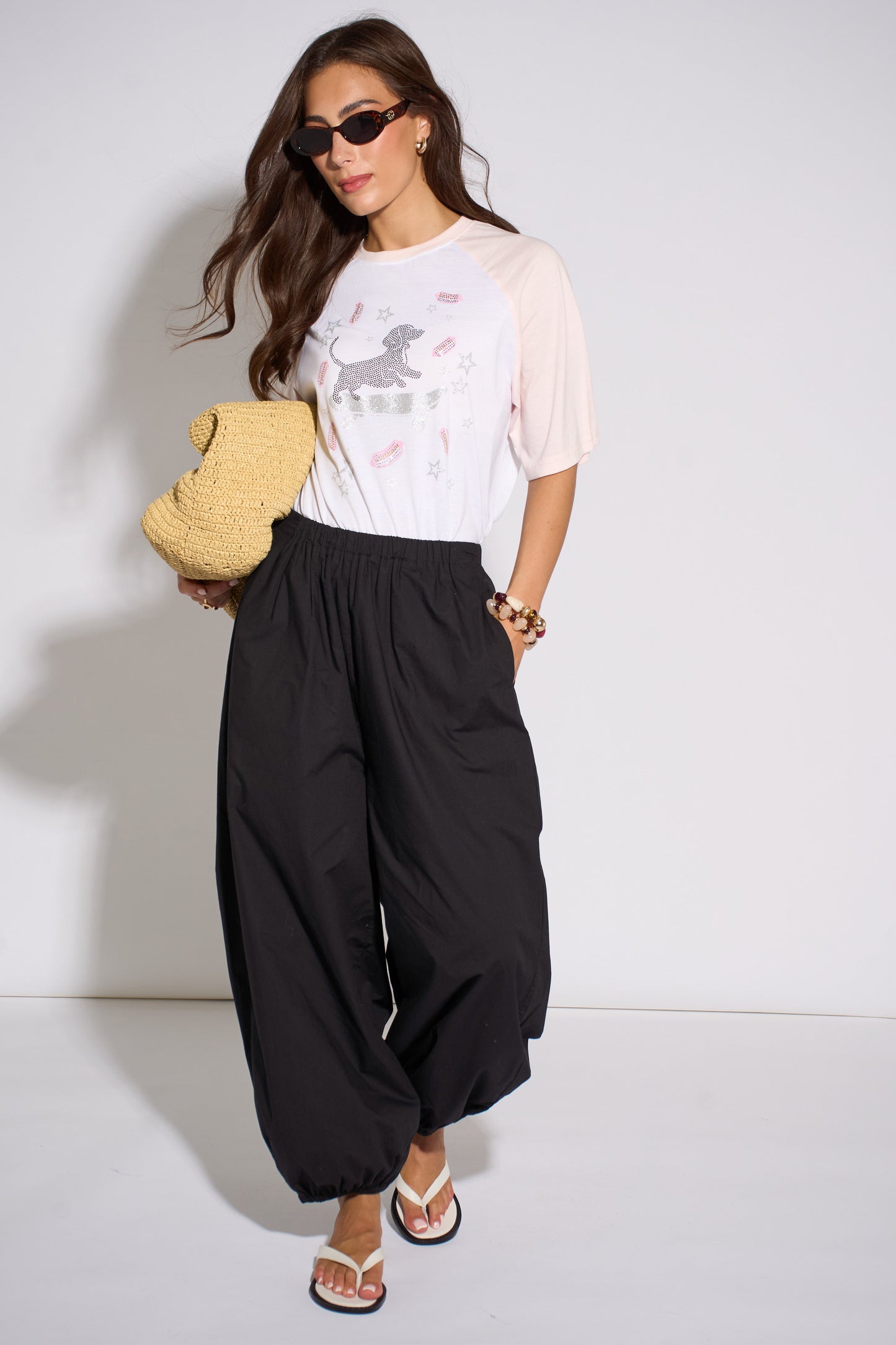 Woman wearing a white t-shirt with graphics and black wide-leg pants, holding a yellow teddy bear.