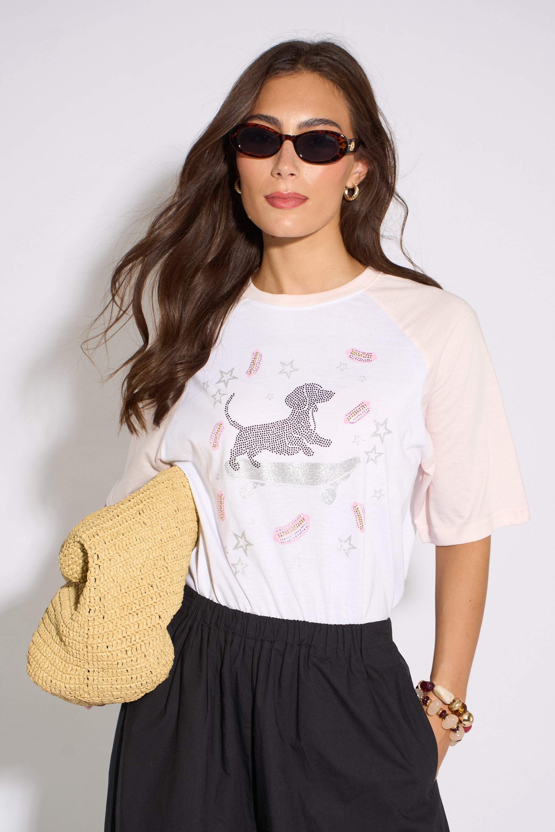Woman wearing a white t-shirt with a dog graphic and sunglasses, holding a yellow bag.