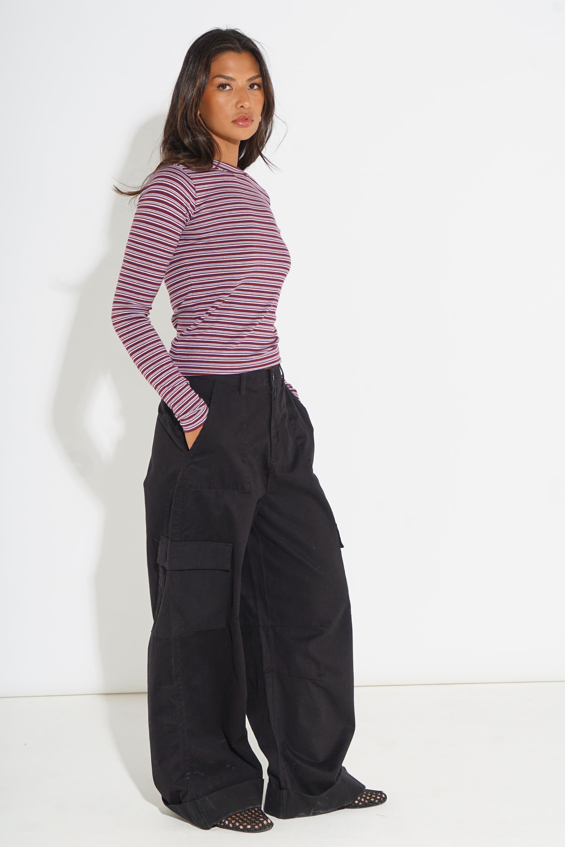 A woman modeling a long-sleeve striped top with dark charcoal cargo pants, standing against a plain white studio background.