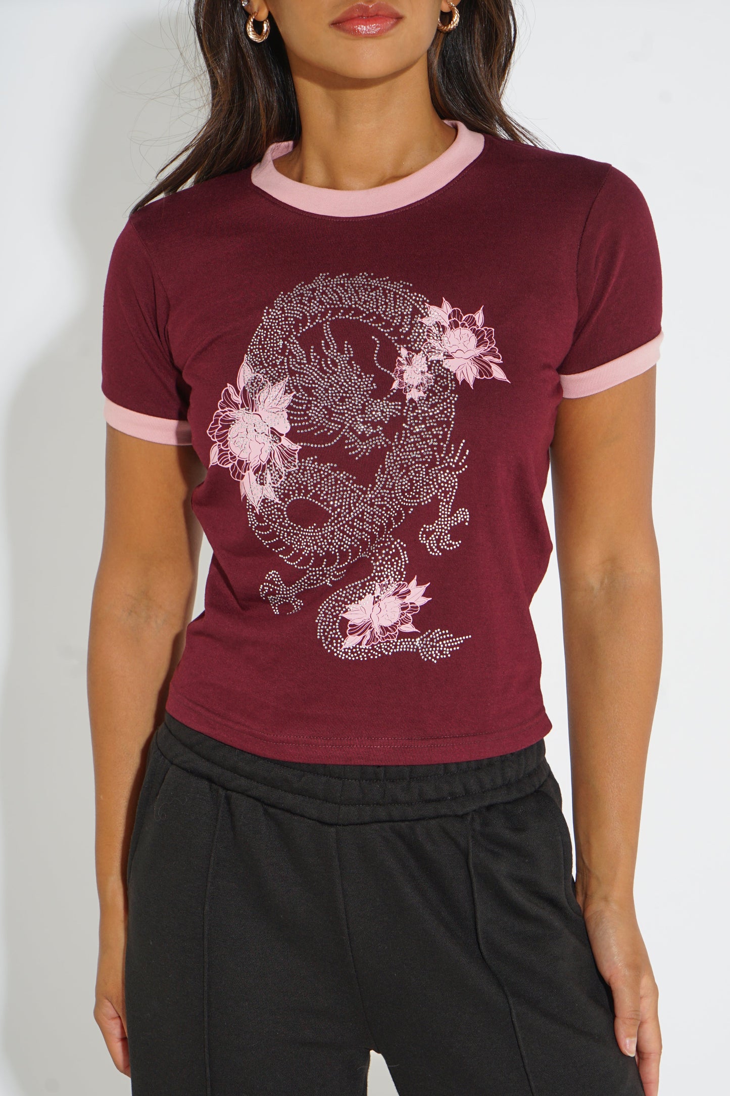 A woman wearing a short-sleeve ringer t-shirt in burgundy with light pink trim and a light pink dragon graphic with cherry blossoms on the front, paired with black sweatpants.