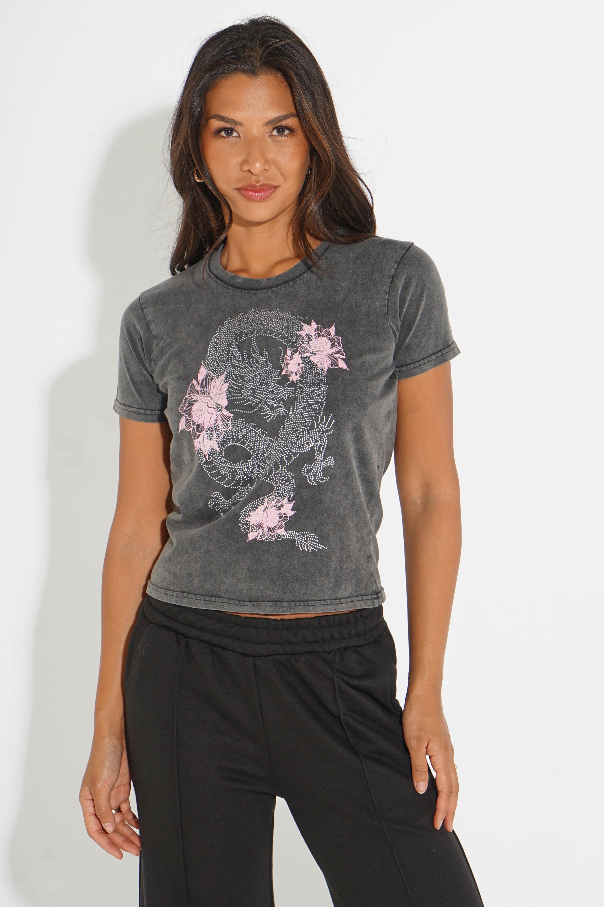 A woman modeling a dark gray washed short-sleeve crop top with a pink and white dragon graphic, paired with black sweatpants, against a plain white studio background.