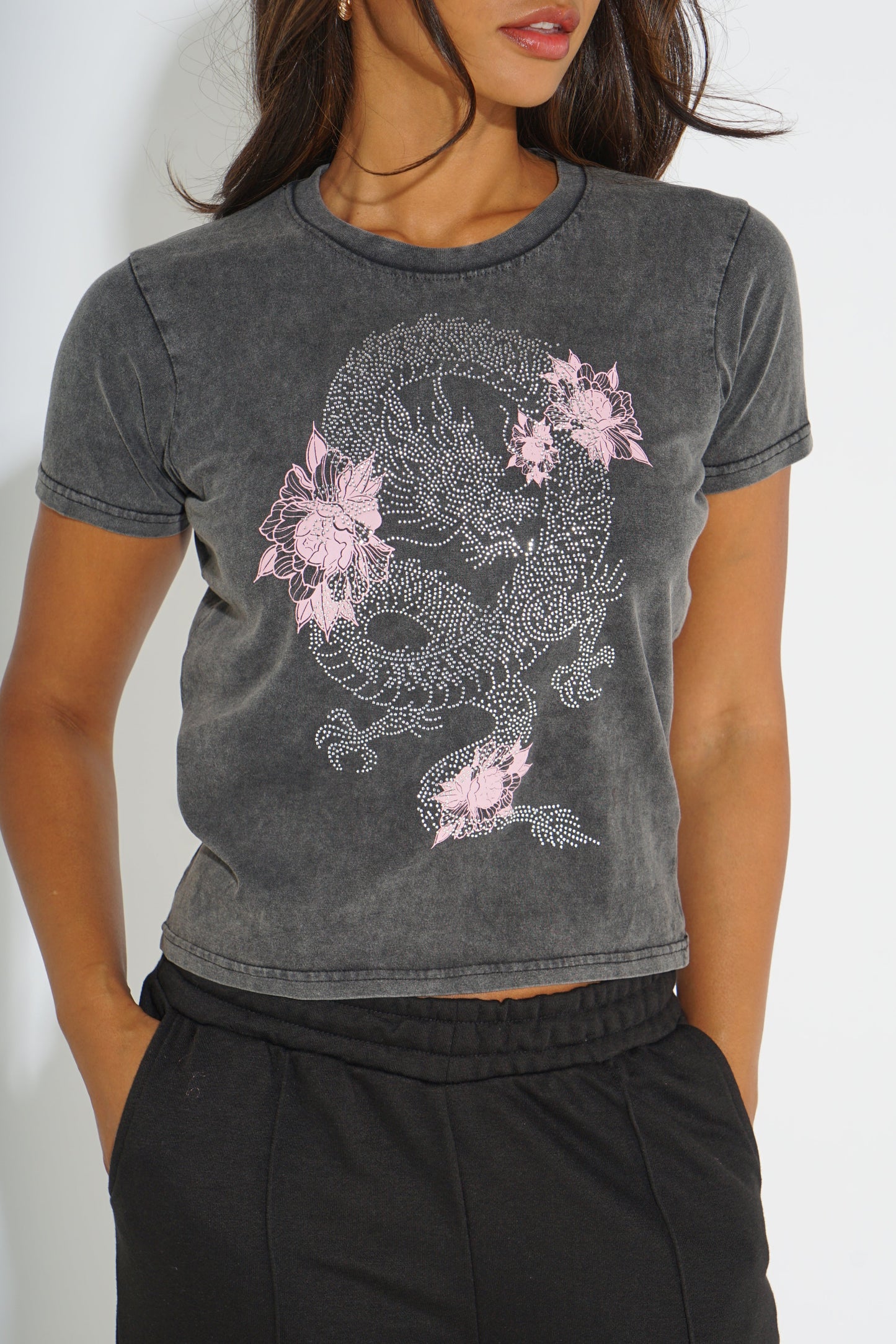 A woman wearing a dark gray mineral-wash cropped t-shirt with a pink and white dragon graphic, paired with black sweatpants.