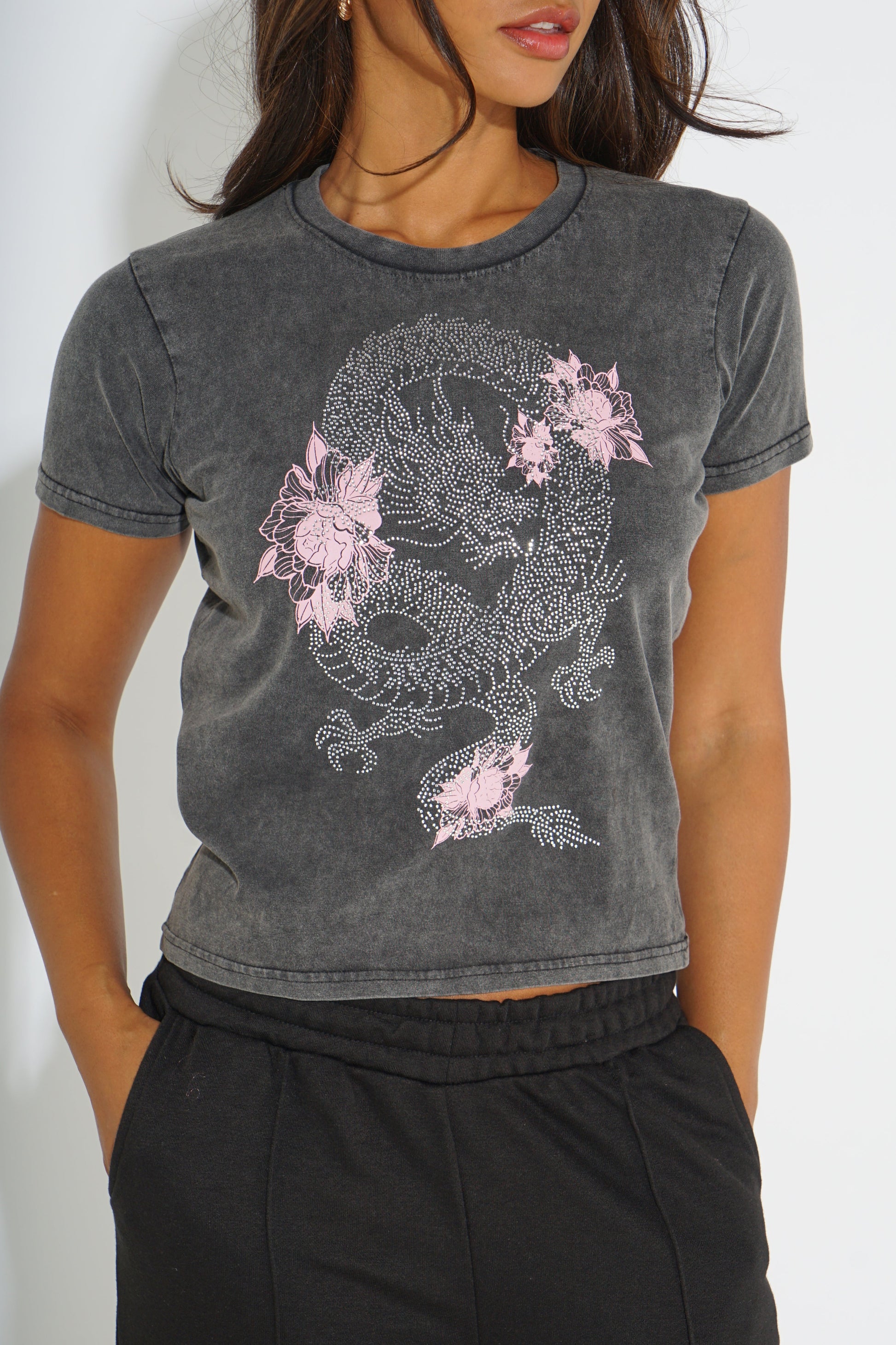 A woman wearing a dark gray mineral-wash cropped t-shirt with a pink and white dragon graphic, paired with black sweatpants.