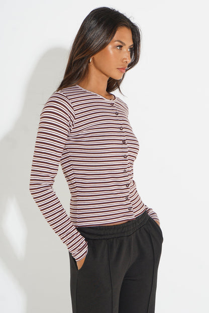 A woman wearing a long-sleeve ribbed button-front top with thin horizontal stripes in dark red and beige, paired with black pants, photographed against a plain light background.