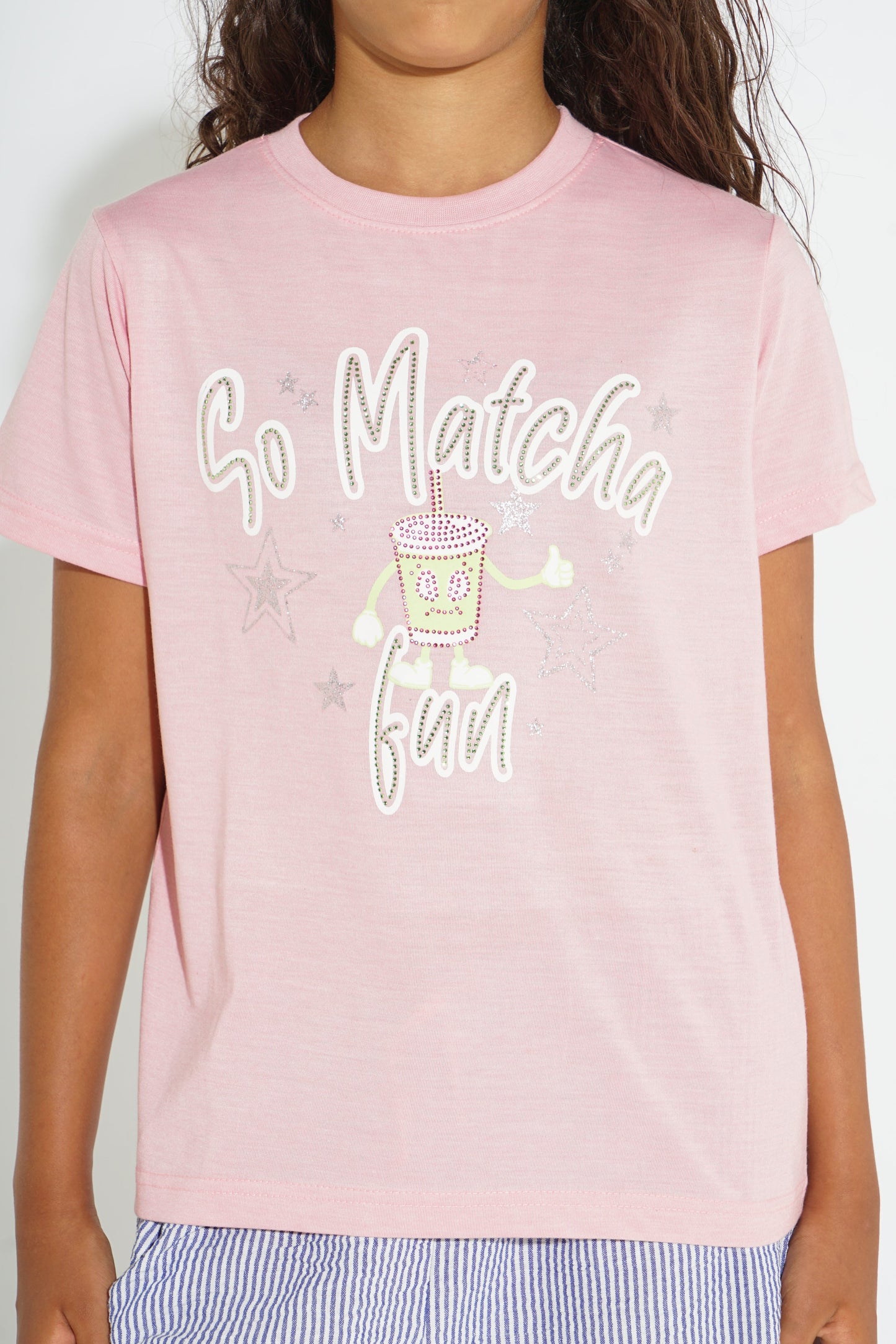 A child wearing a light pink short-sleeve t-shirt with a rhinestone-embellished graphic that reads 'So Matcha Fun' with a small matcha drink illustration in the center.