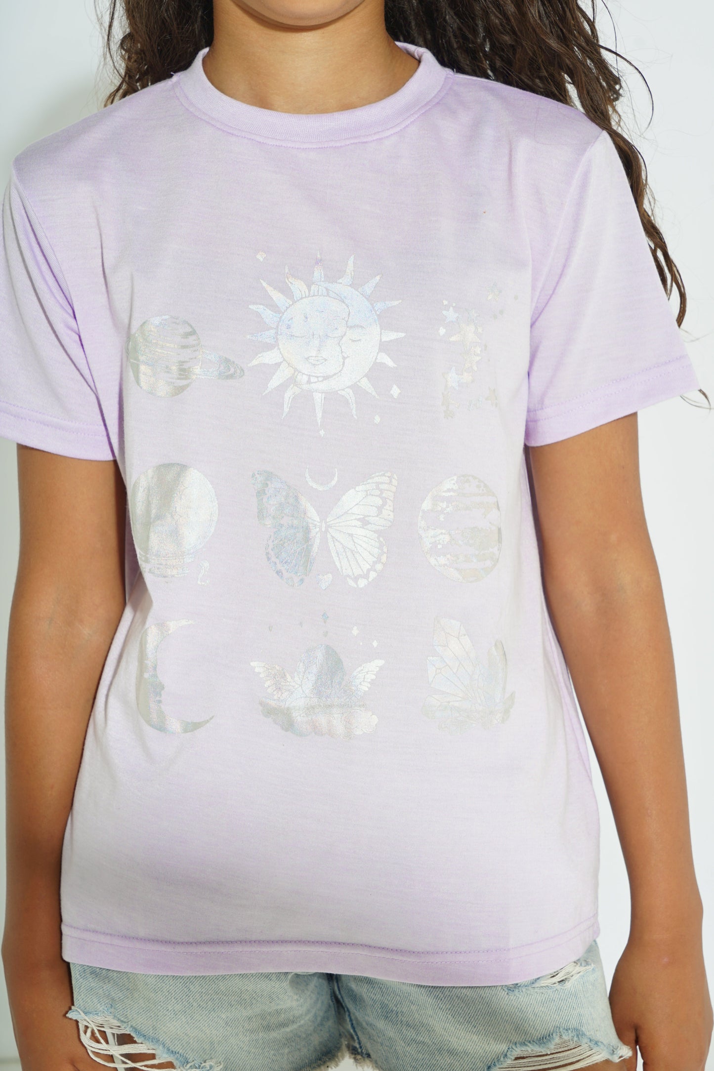 A person wearing a light lavender short-sleeve T-shirt with a white celestial and nature graphic print on the front, paired with light-wash denim shorts.