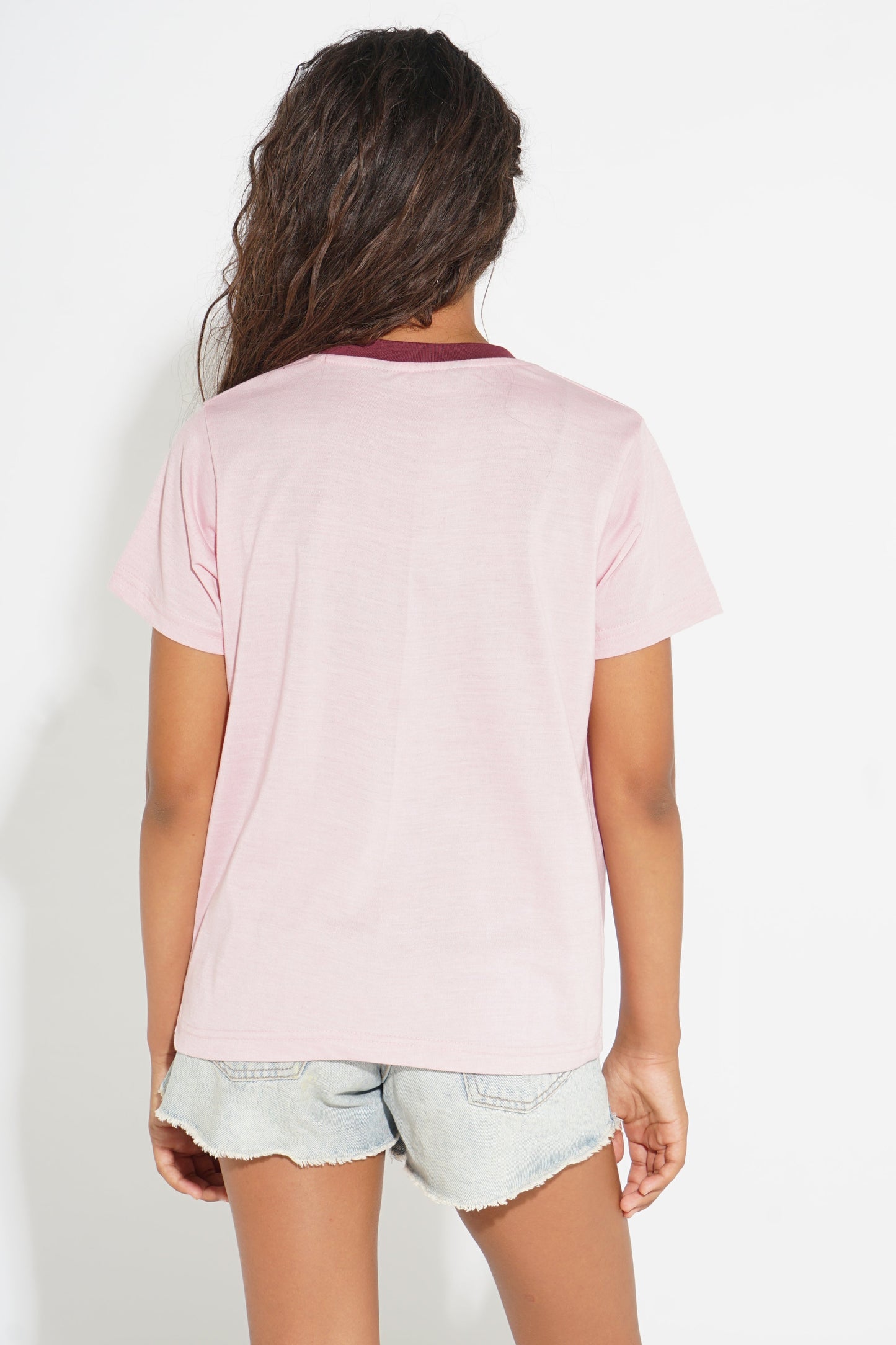A girl viewed from behind wearing a light pink short-sleeve t-shirt with a contrasting dark red collar and light denim shorts, set against a plain white background.