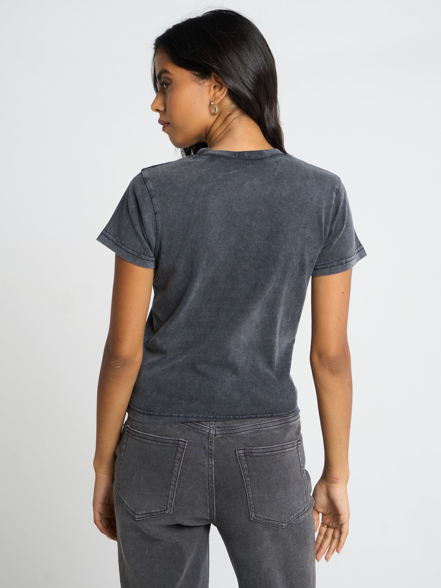 A woman shown from the back wearing a dark gray washed short-sleeve t-shirt and matching gray jeans against a light gray studio background.