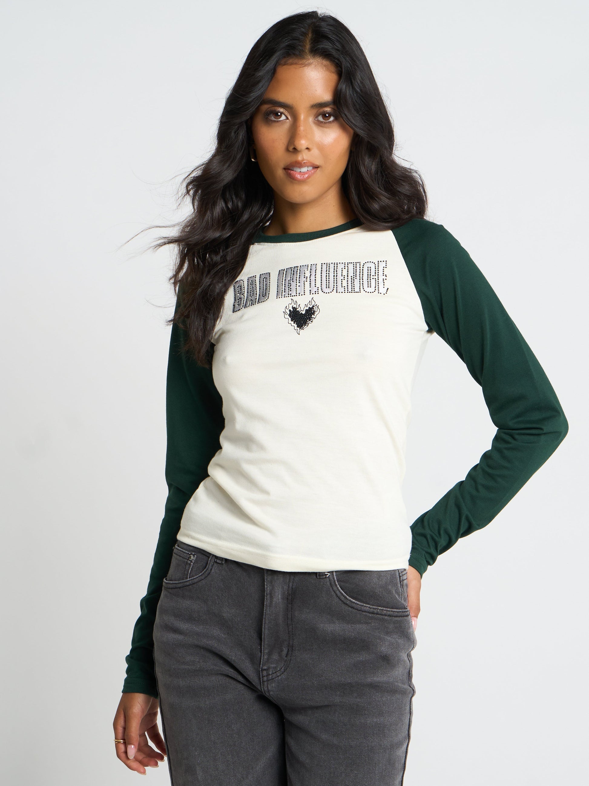 A woman modeling a long-sleeve raglan t-shirt with an off-white body and dark green sleeves. The shirt features the text 'BAD REFLECTION' and a black bird graphic on the chest.