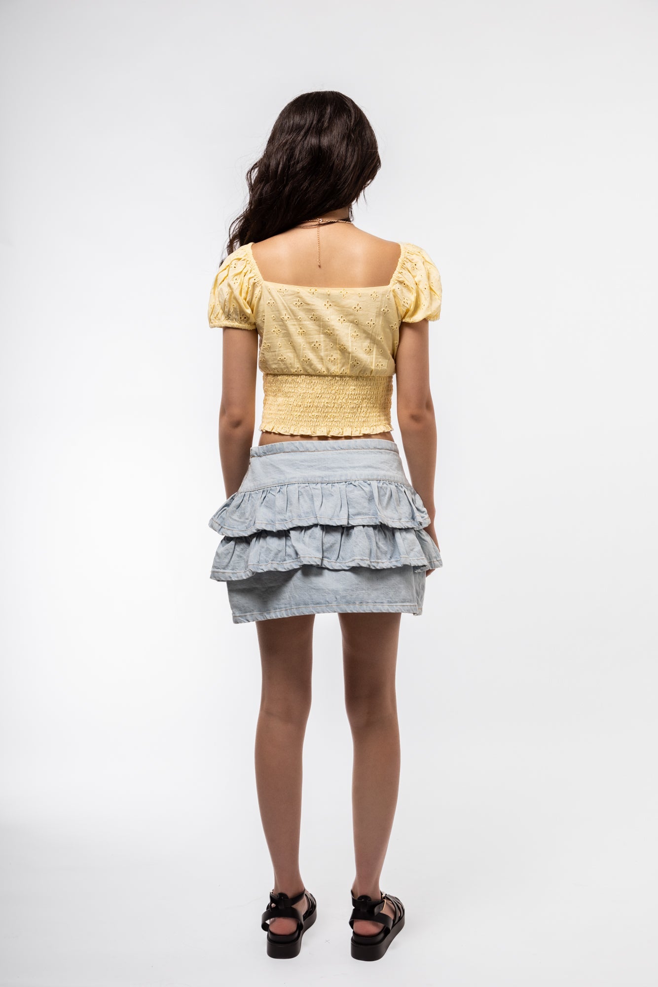 Back image of wrap ruffle skirt in denim with clean waistband and tiered ruffle peeking around.


