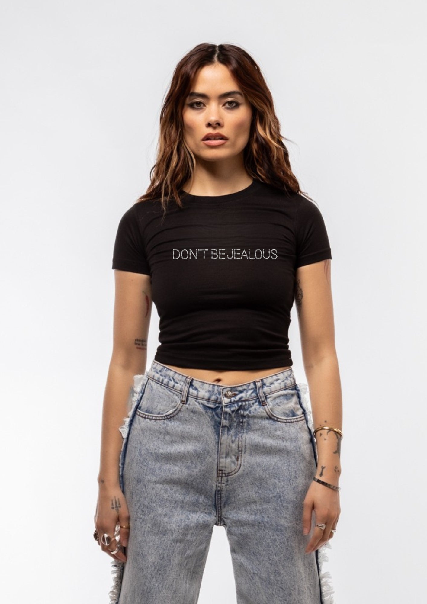 Woman wearing a black t-shirt with 'DON'T BE JEALOUS' text and high-waisted jeans on a white background