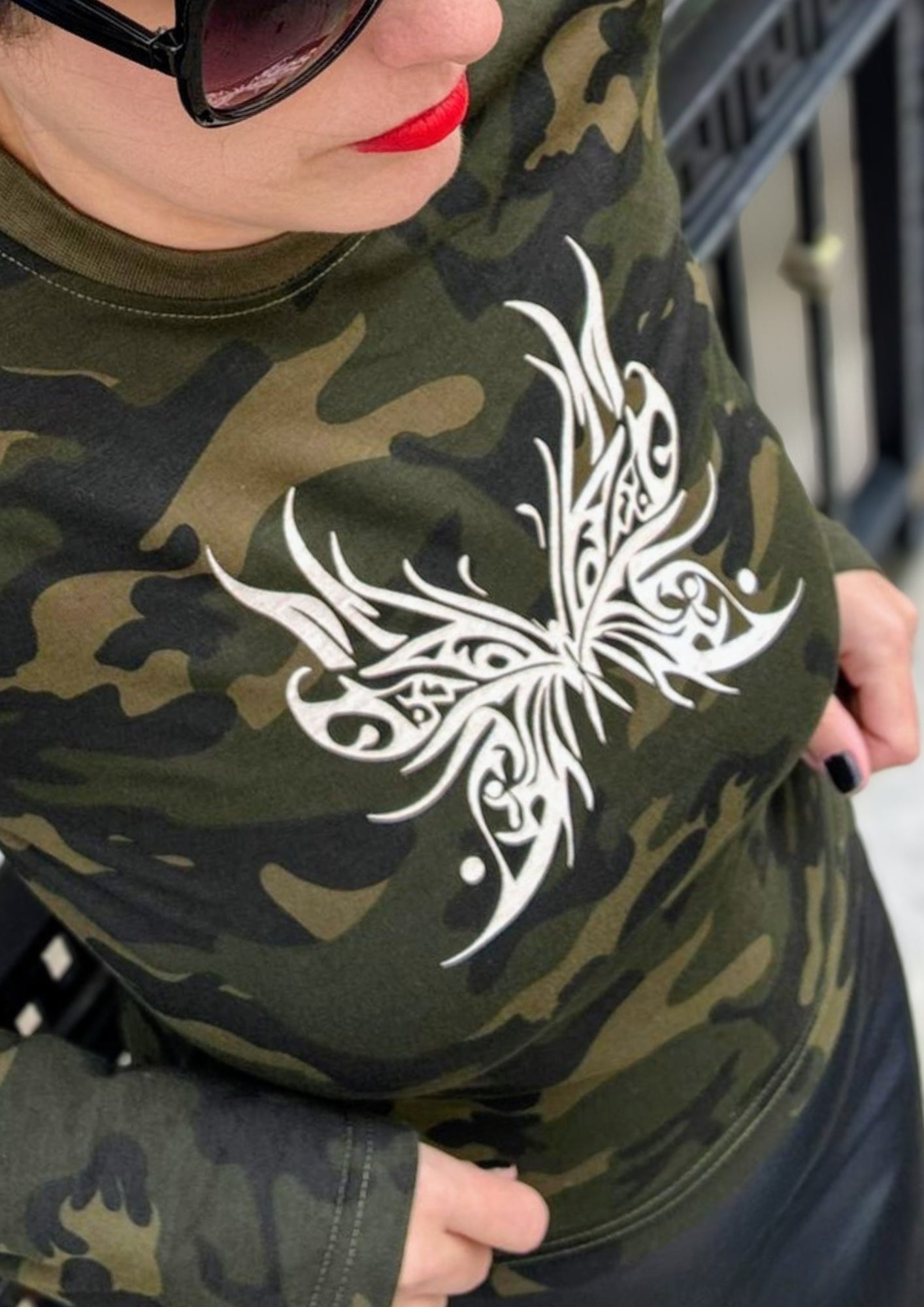 Camouflage t-shirt with a white butterfly design worn by a person.