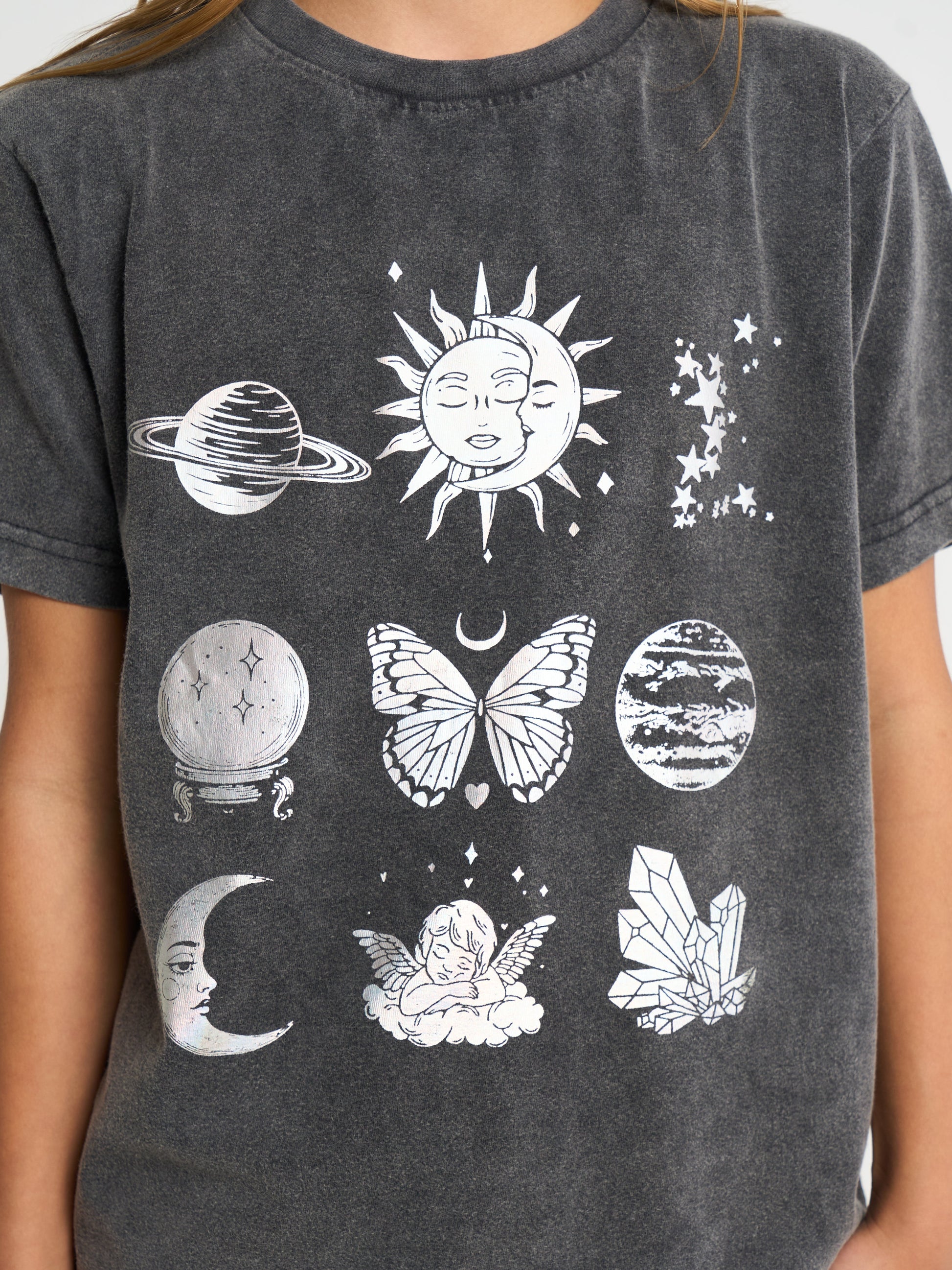 A close-up of a person wearing a dark gray acid-wash t-shirt with a white celestial graphic print featuring a sun, moon, crystals, and a butterfly.