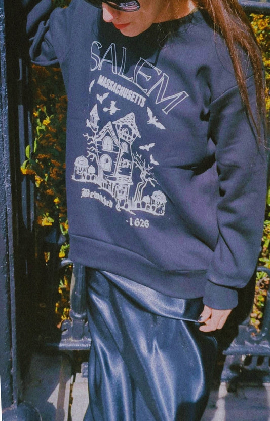 Person wearing a black sweatshirt with 'Salem, Massachusetts' print outdoors.
