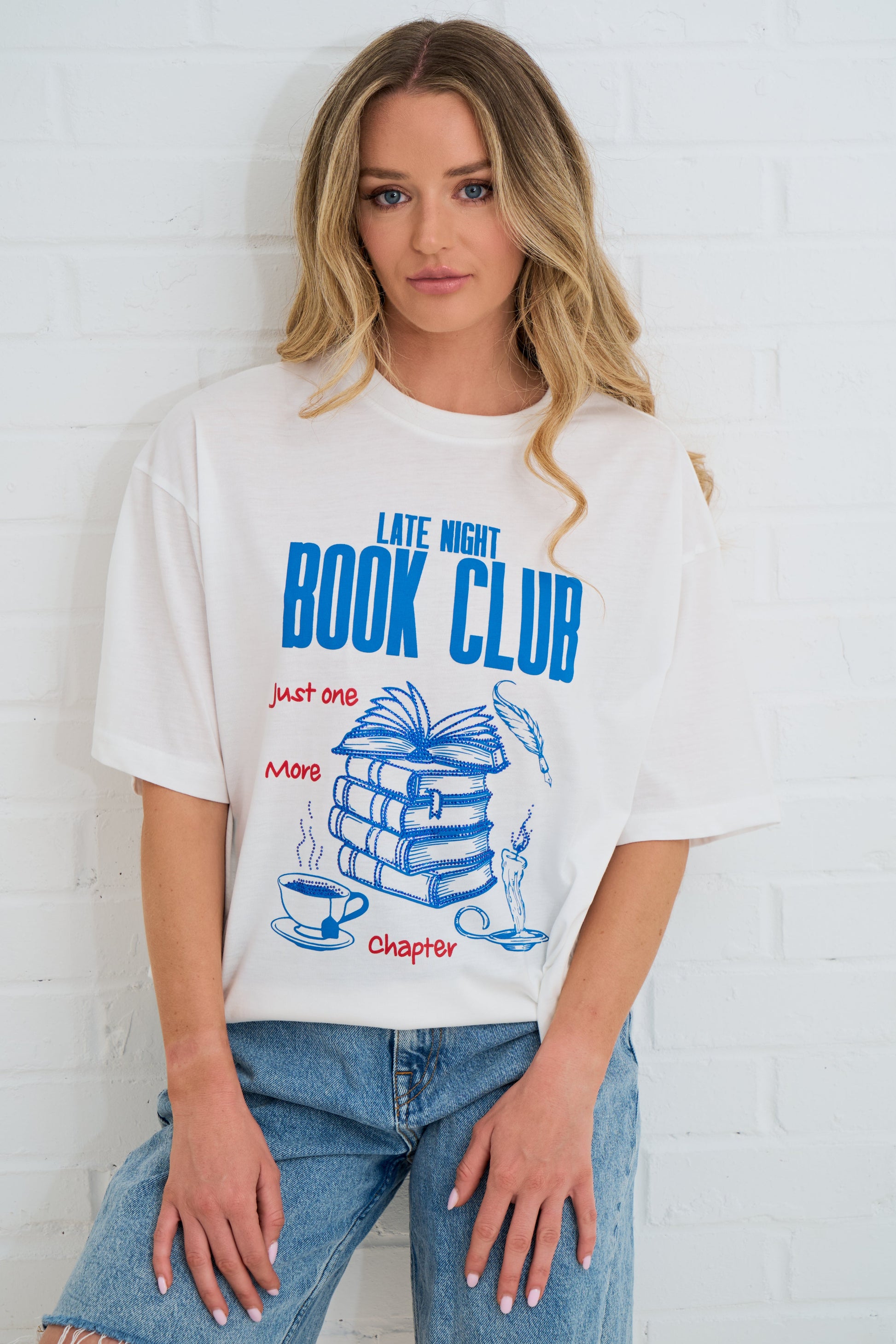 Person wearing a 'Late Night Book Club' t-shirt with a graphic design against a white brick wall.