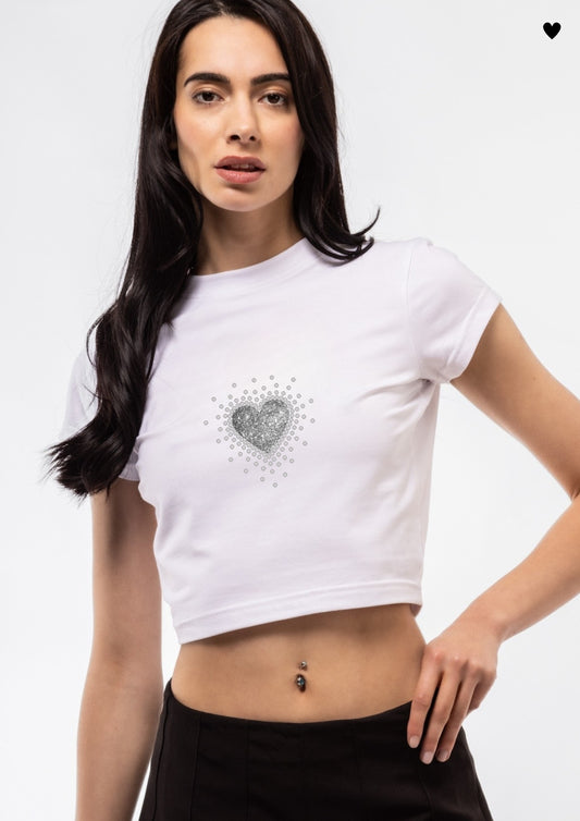 Woman wearing a white crop top with a heart design on a plain background