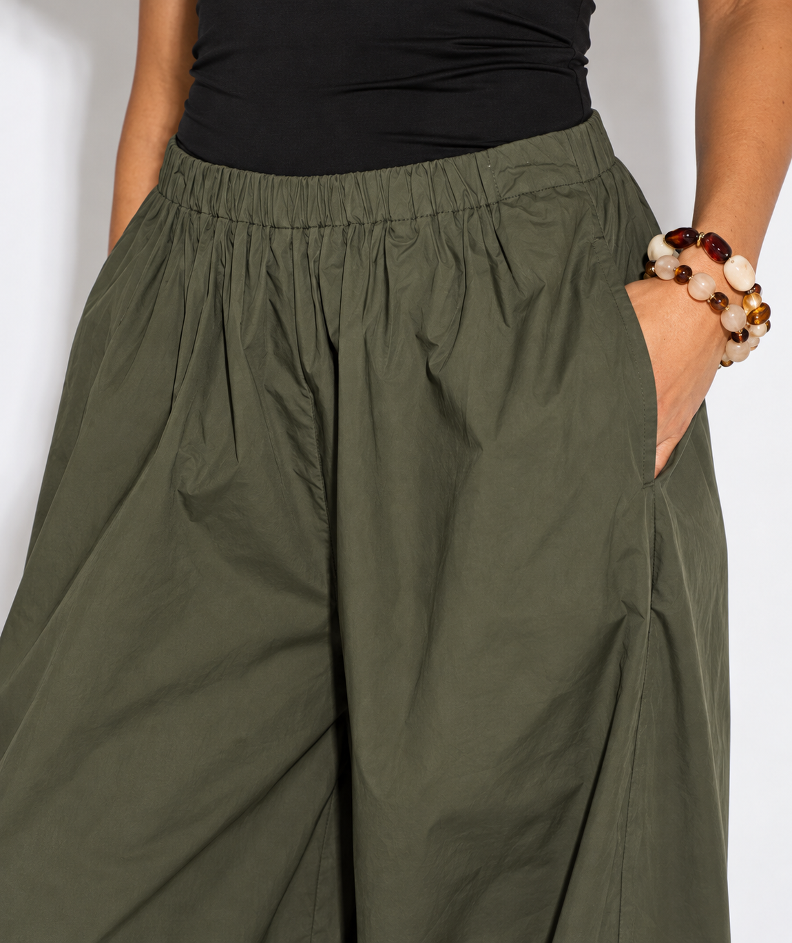 Olive green wide-leg pants with an elastic waistband and side pockets, shown on a model wearing a black top and beaded bracelets.