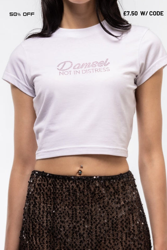 Person wearing a white crop top with 'Damsel Not In Distress' text and a black sequin skirt.