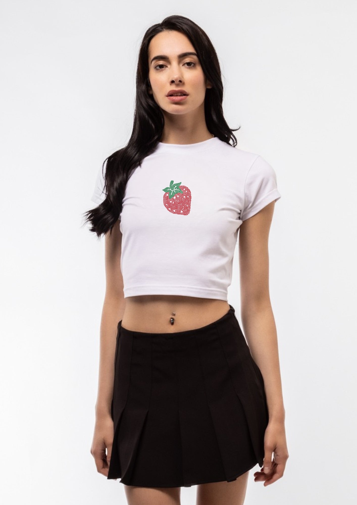 Model  wearing a white crop top with a strawberry design and a black pleated skirt on a white background