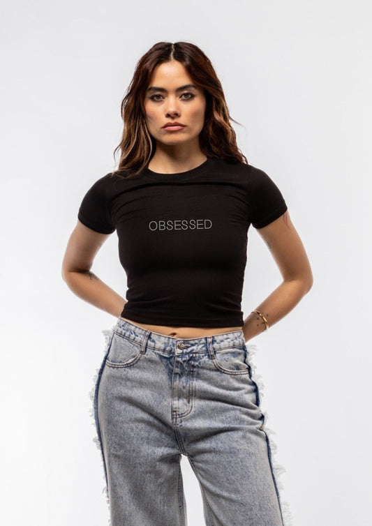 Woman wearing a black t-shirt with 'OBSESSED' text and high-waisted jeans on a white background