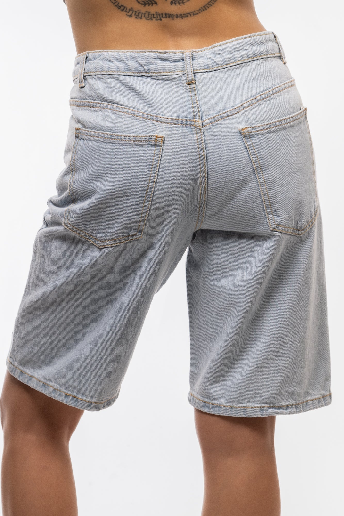 Rear shot of stud denim jorts with metal stud accents on pockets and frayed hems.

