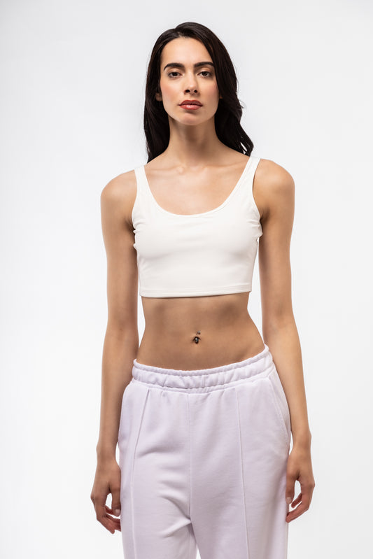 Woman wearing a white tank top and light purple sweatpants on a white background