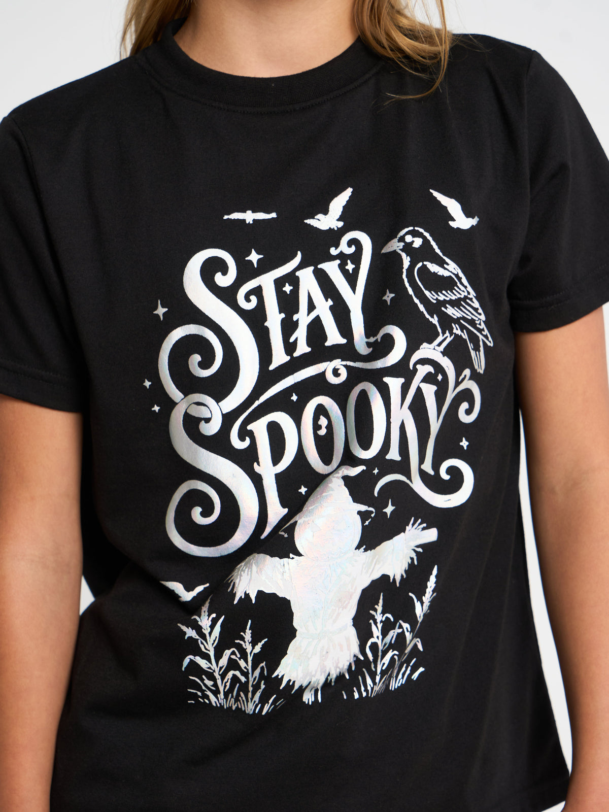 A person wearing a black short-sleeve T-shirt with a large white 'Stay Spooky' graphic featuring a bird, ghost, and stars.