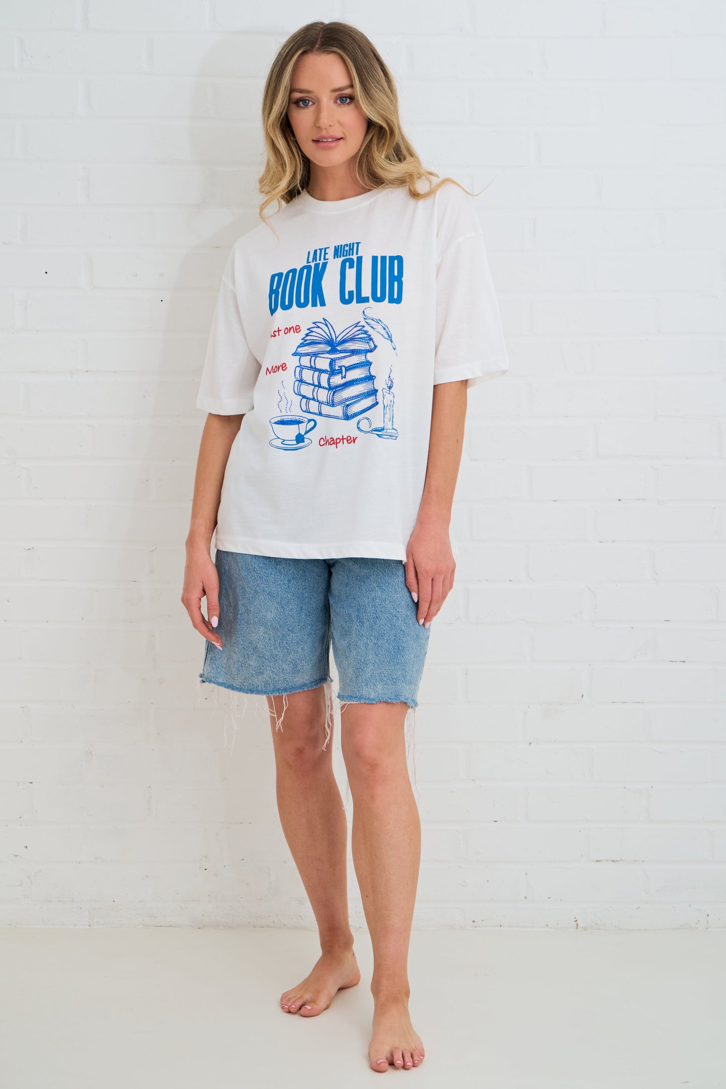 Woman wearing a white t-shirt with blue graphics and text against a white brick wall.