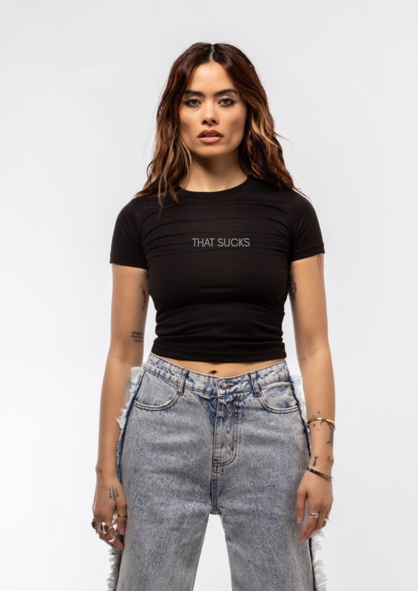 Woman wearing a black t-shirt with 'THAT SUCKS' text and high-waisted jeans on a white background