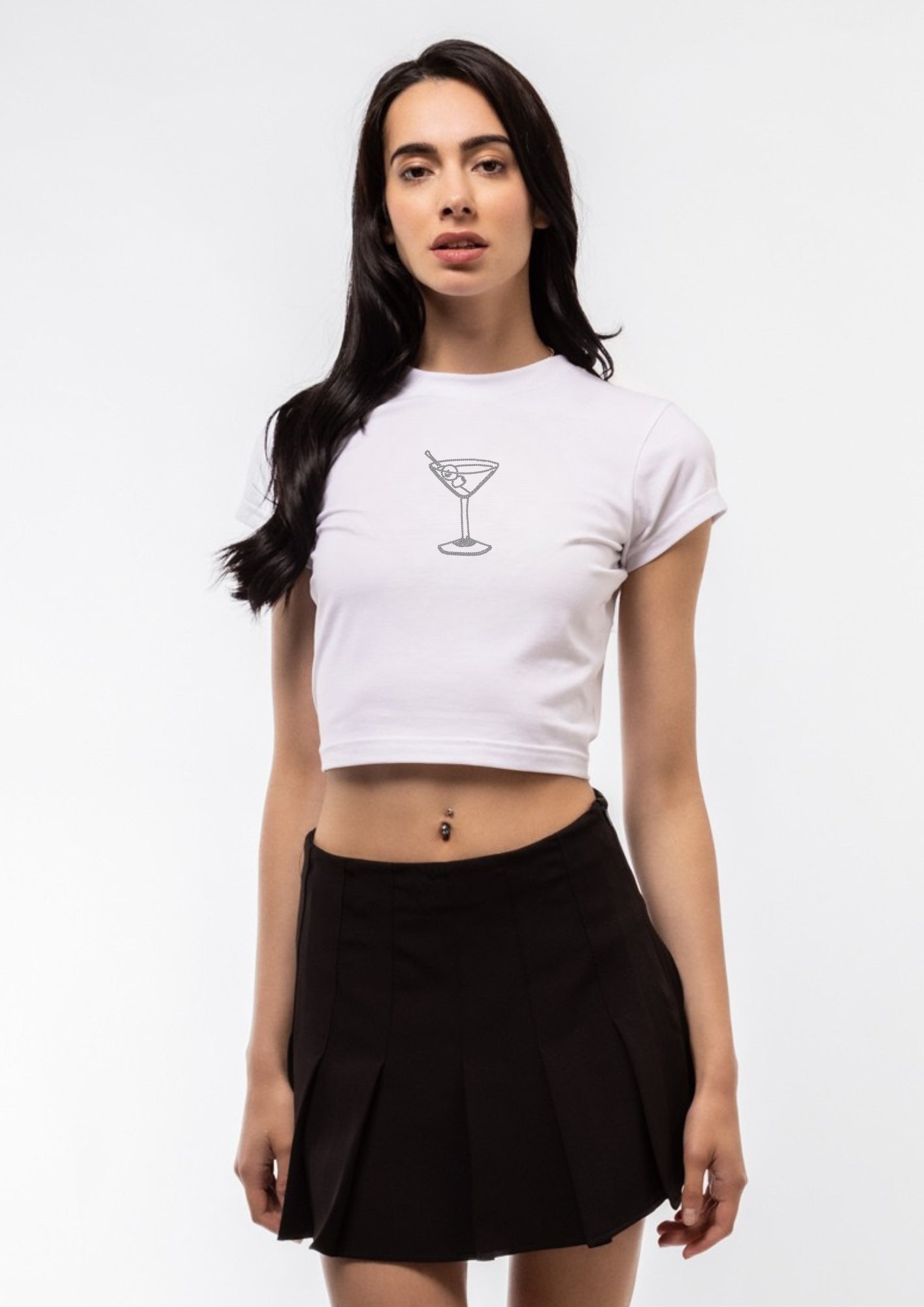 Woman wearing a white crop top with a MARTINI COCKTAIL GLASS graphic design and a black pleated skirt on a white background