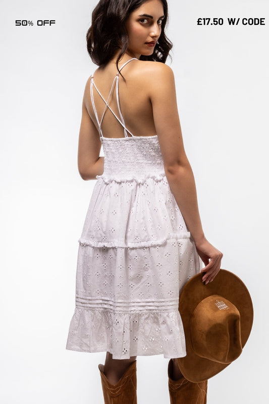 Woman wearing a white dress with thin straps, holding a brown hat on a white background.