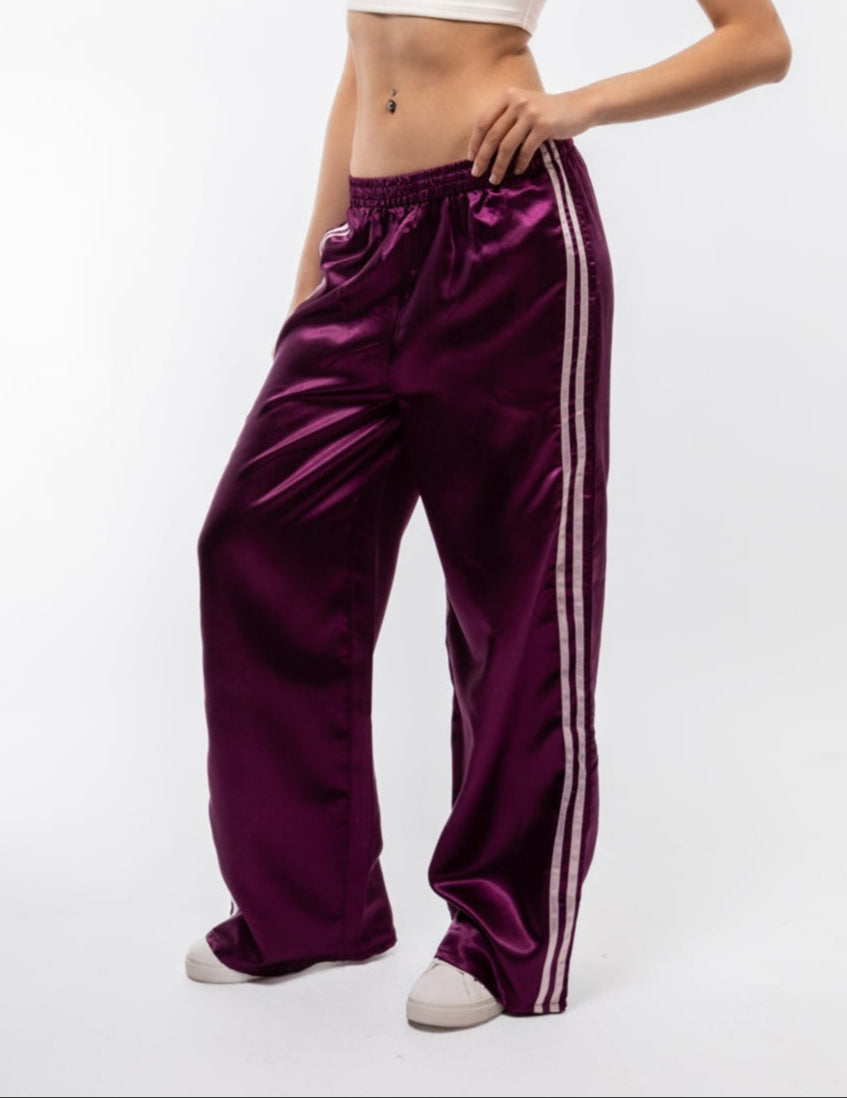 Woman wearing a white top and purple satin pants with white stripes on a white background