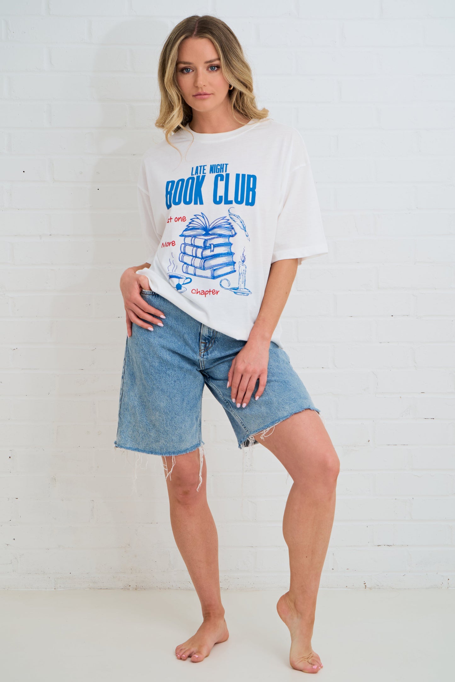 Woman wearing a white t-shirt with text and graphics, paired with denim shorts, against a white background.